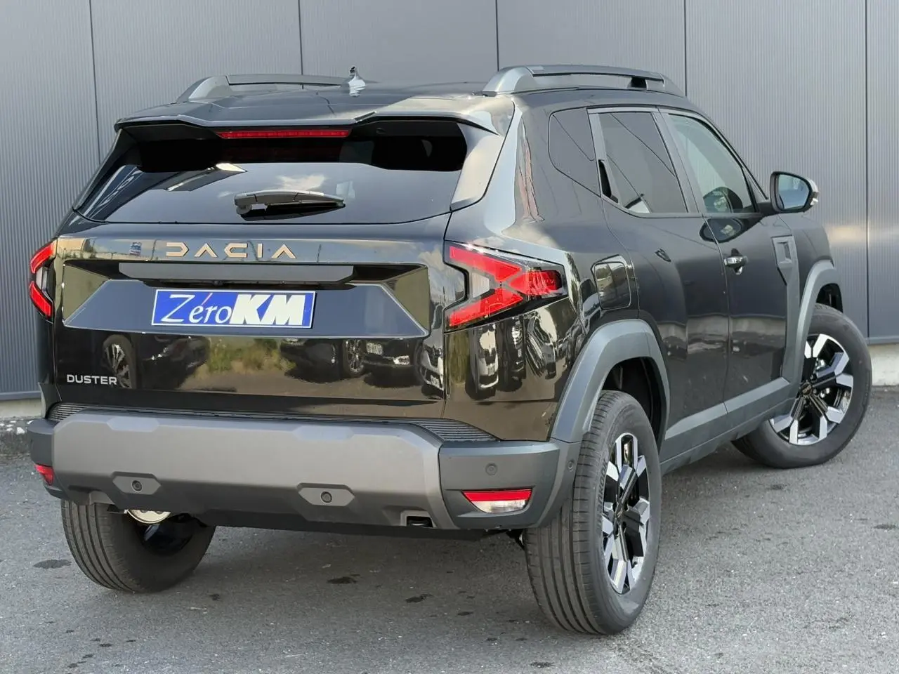 Vue 3/4 arrière droite du Dacia Duster noir nacré avec jantes alliage et barres de toit visibles.