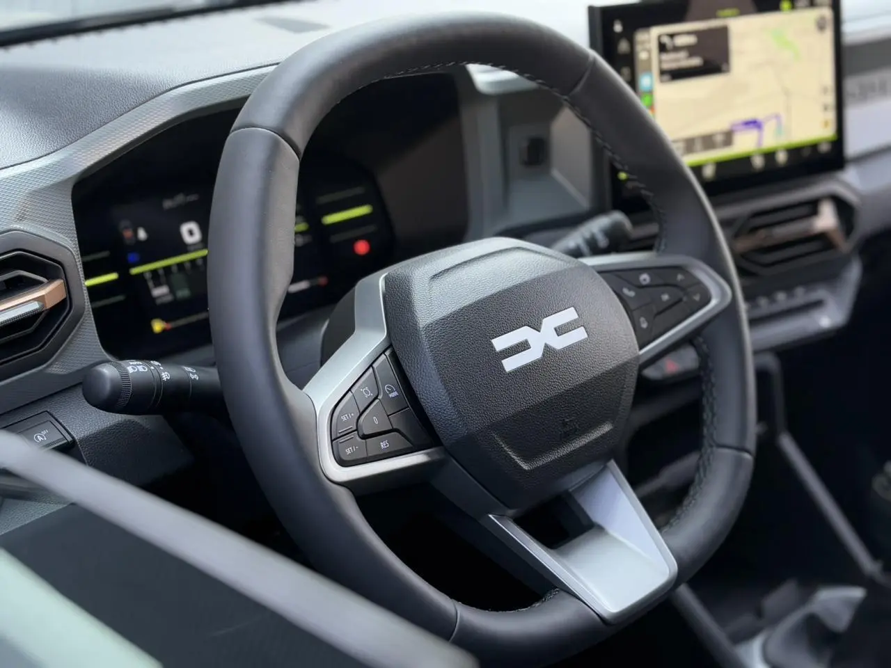 Vue rapprochée du volant noir du Dacia Duster 2025 avec commandes intégrées et écran tactile GPS en arrière-plan.