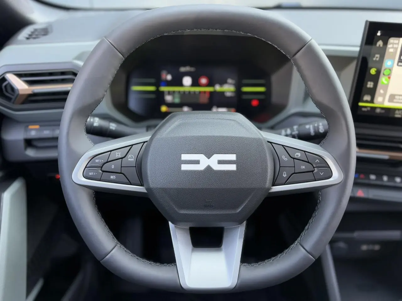 Volant noir du Dacia Duster 2025 avec commandes intégrées, tableau de bord digital et écran tactile visible en arrière-plan.