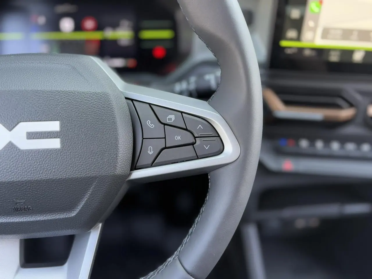 Gros plan sur le volant droit en cuir noir du Dacia Duster 2025 avec commandes intégrées et tableau de bord flou.