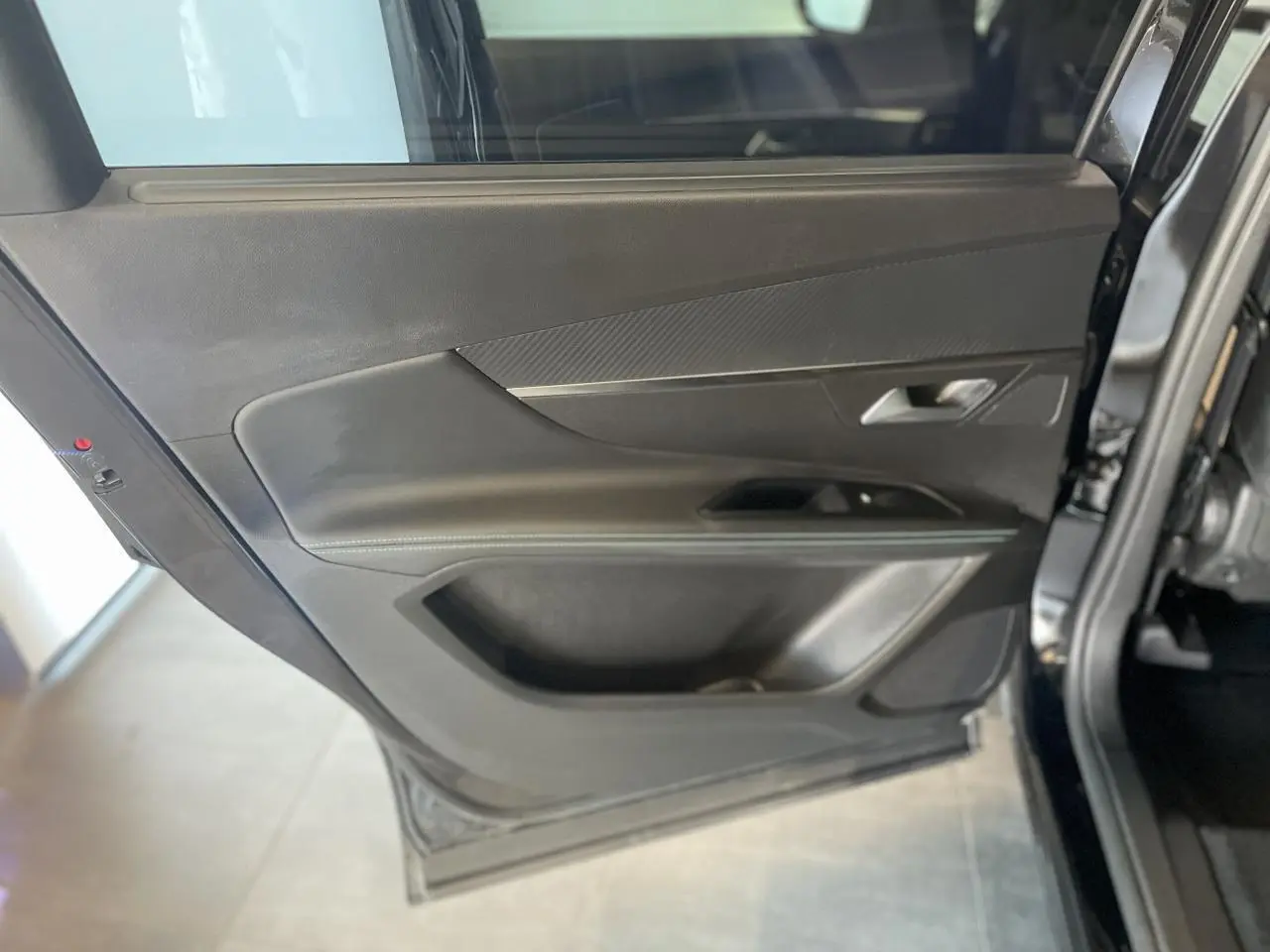 Gros plan sur la porte arrière gauche noire métallisée du Peugeot 5008 2024 avec insert carbone et poignée grise.