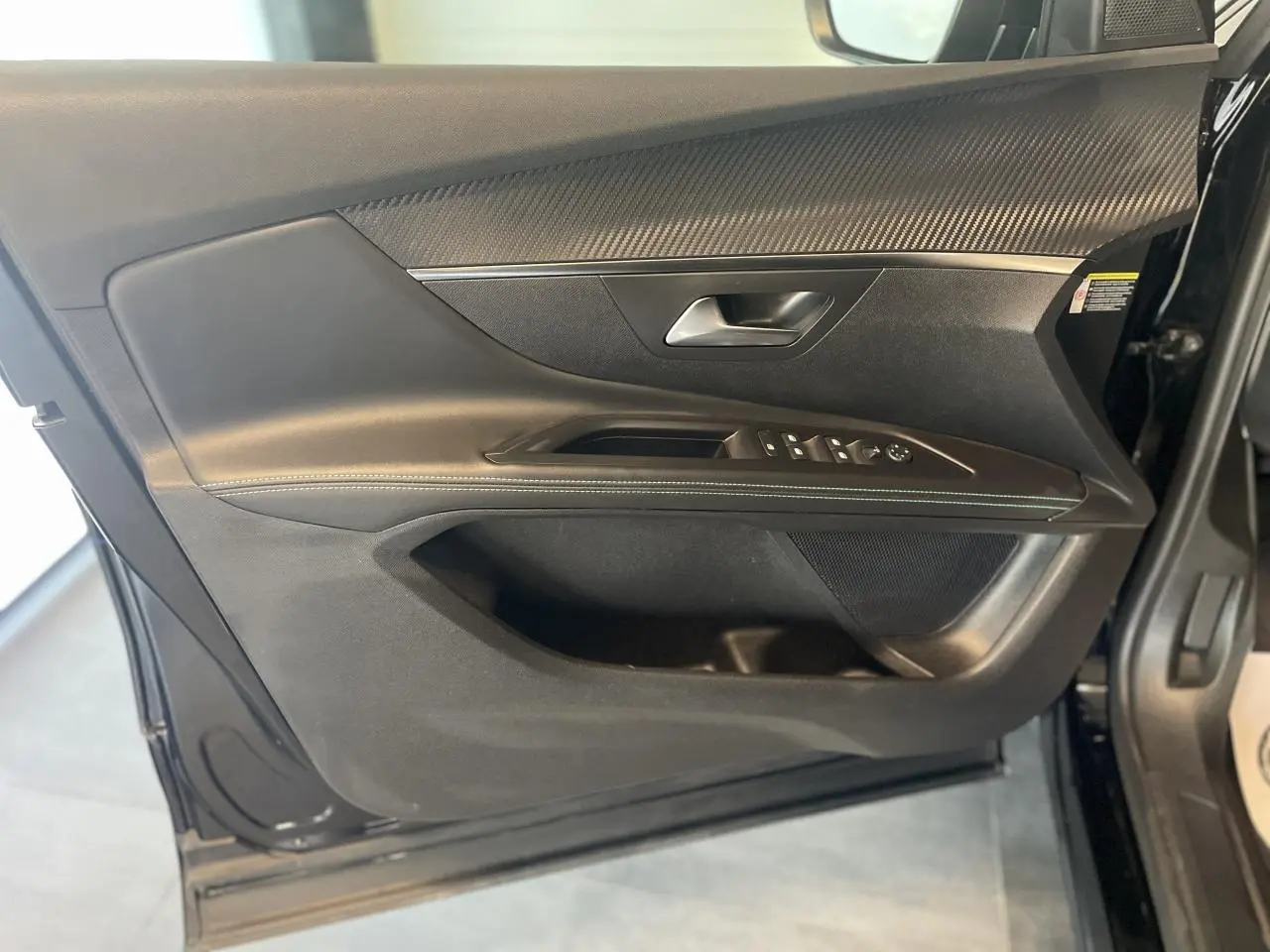 Porte côté gauche ouverte du Peugeot 5008 noir métallisé, montrant les commandes de vitres et insert décor carbone.