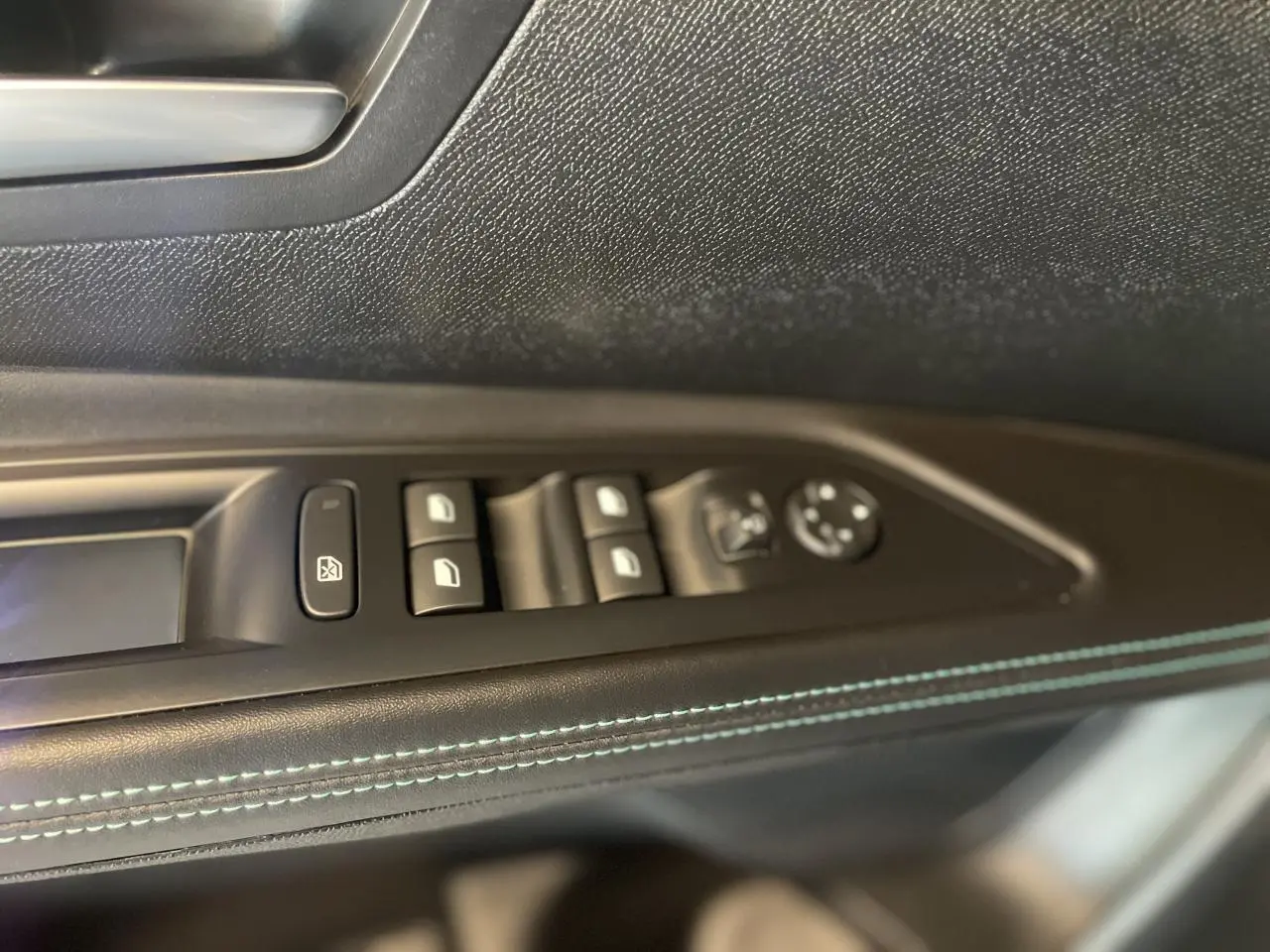 Gros plan sur la commande des vitres côté conducteur du Peugeot 5008 2024 avec surpiqûres bleues sur panneau de porte noir.
