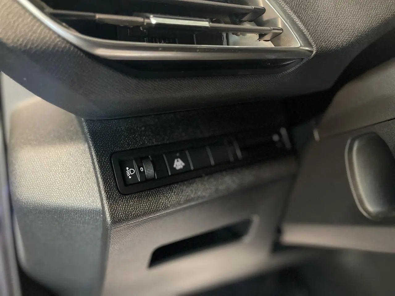 Détail du tableau de bord côté gauche du Peugeot 5008 2024 avec commande de réglage des phares et texture noire.