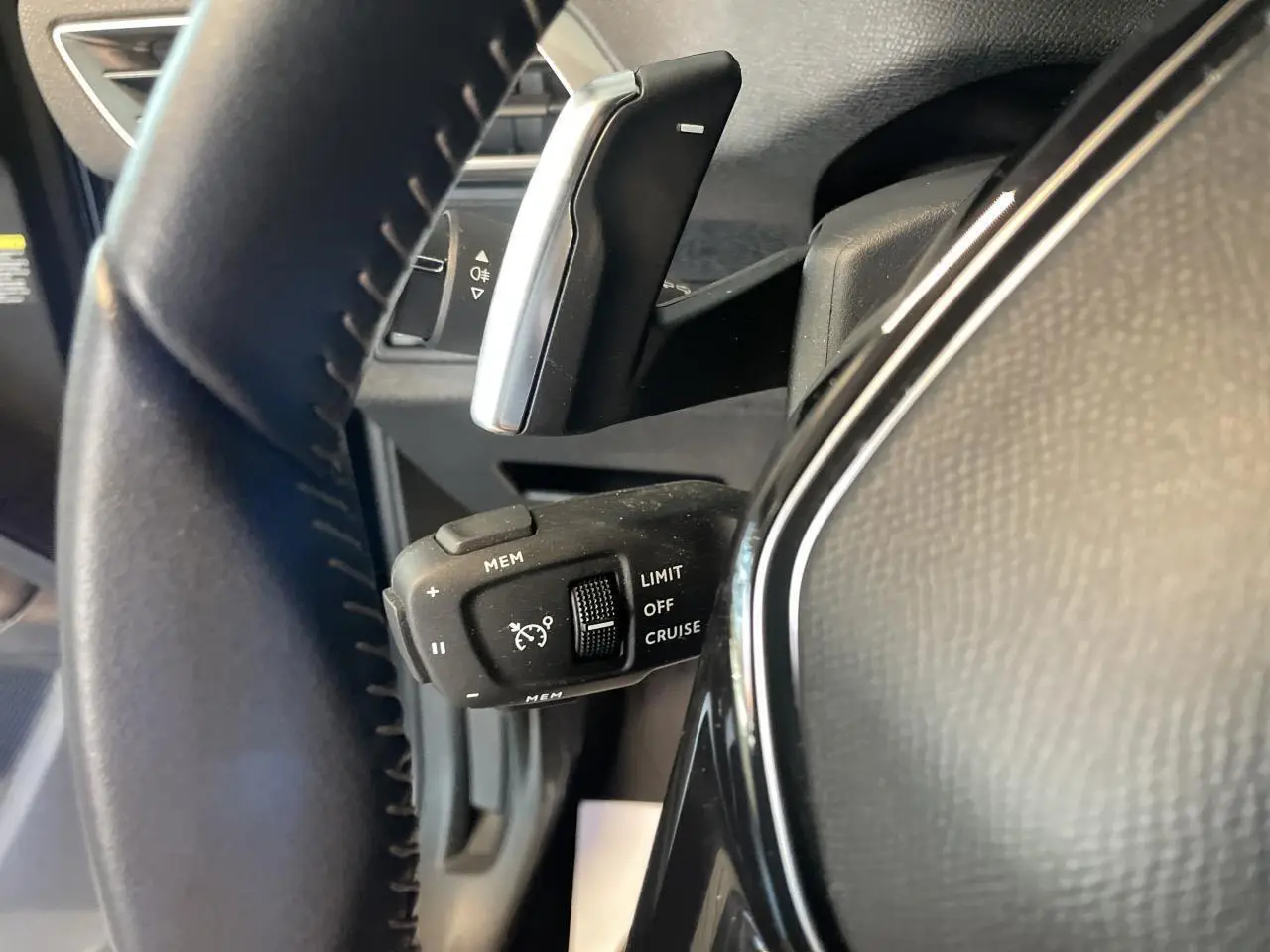 Gros plan sur la commande de régulateur de vitesse à gauche du volant noir du Peugeot 5008 2024 finition Allure Pack.