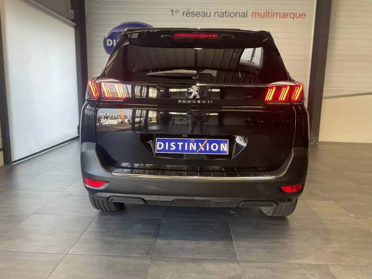 Vue arrière d'un Peugeot 5008 noir métallisé avec feux arrière LED 3D et logo Peugeot visible en intérieur showroom.