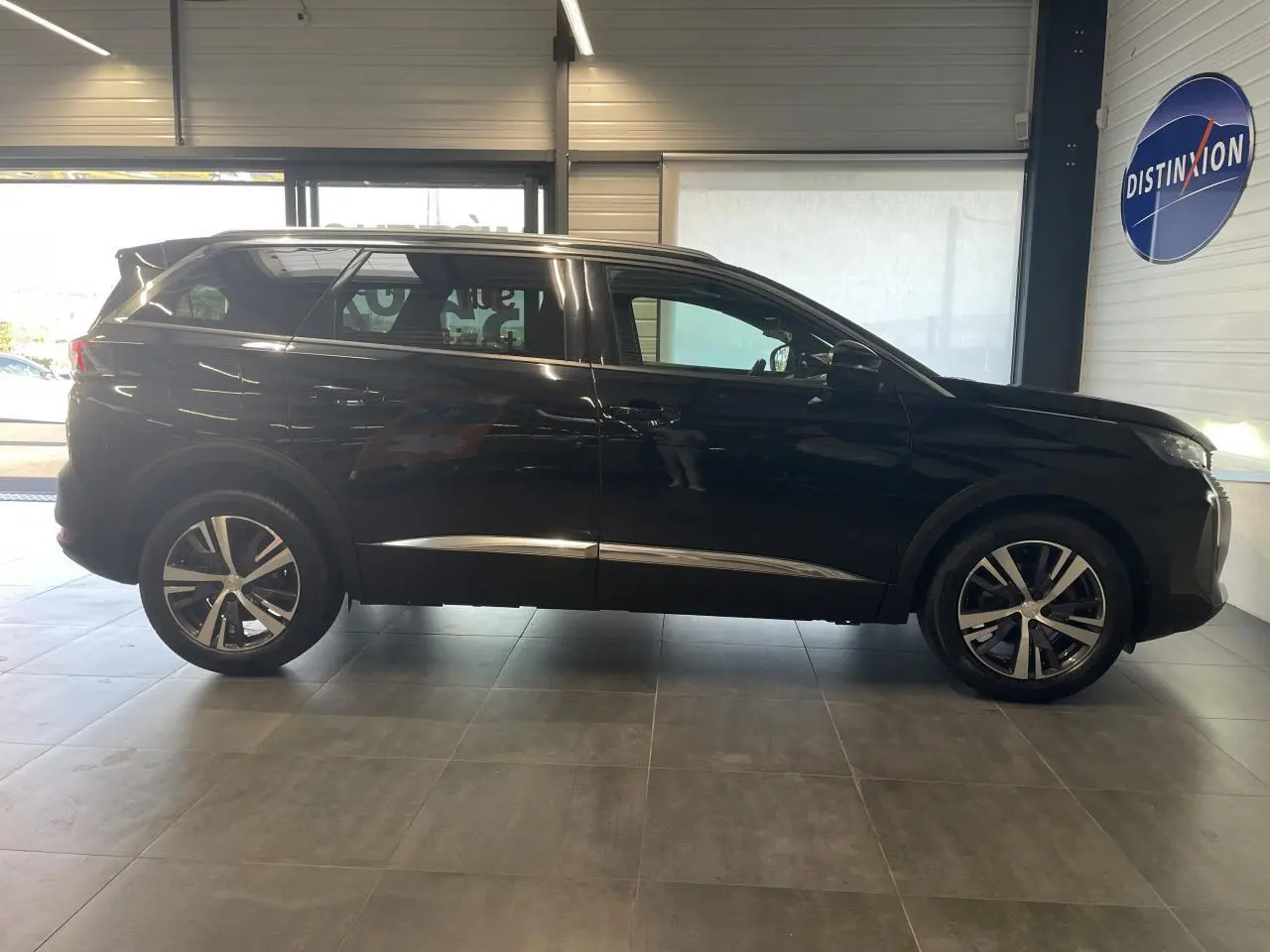 Profil droit du Peugeot 5008 noir métallisé 2024 avec jantes alliage bi-ton et barres de toit profilées en aluminium.