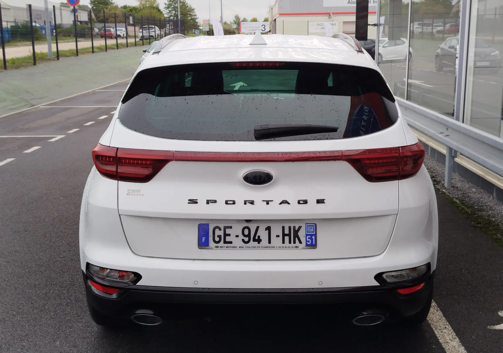 Vue arrière d'un KIA Sportage blanc 2022 avec feux LED reliés et double sortie d'échappement visible sur parking.