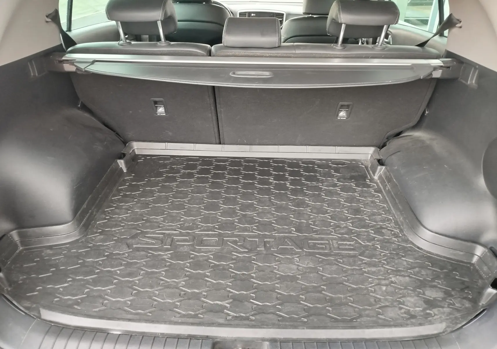 Coffre ouvert du Kia Sportage blanc, vue intérieure arrière montrant le tapis de coffre noir avec logo Sportage.