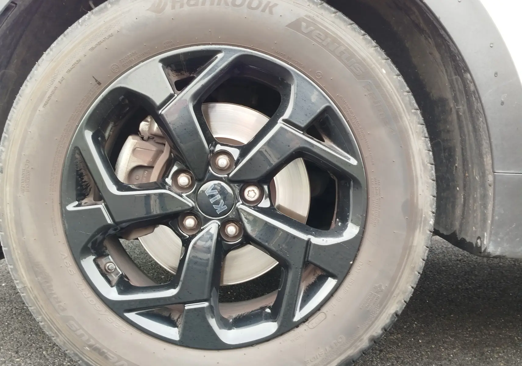 Gros plan sur la roue avant droite du Kia Sportage blanc 2022 avec jante alliage noire et logo Kia central.