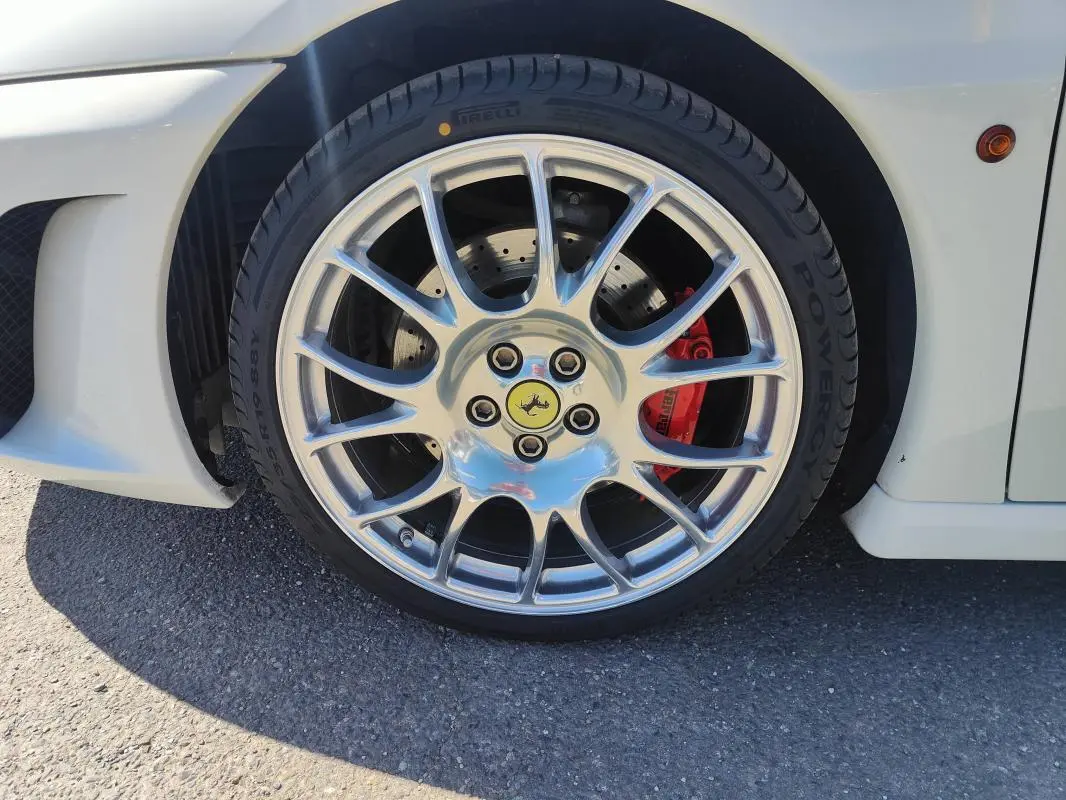 Gros plan sur la roue avant droite d'une Ferrari F430 Spider blanche, avec étrier de frein rouge et jante argentée brillante.