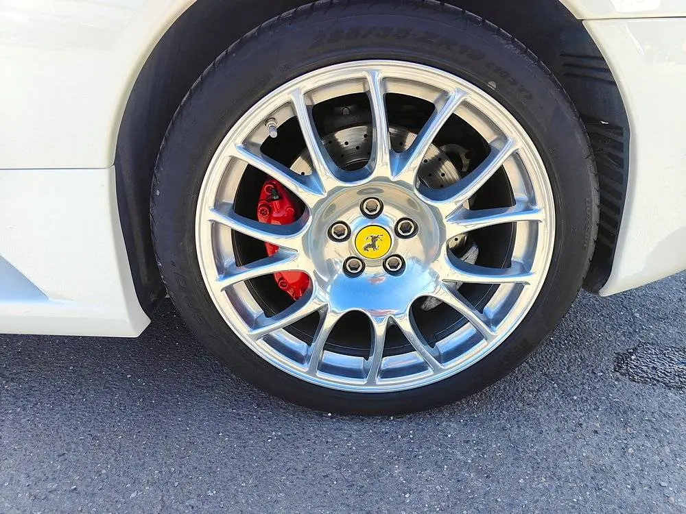 Gros plan sur la roue avant gauche d'une Ferrari F430 Spider blanche avec étrier de frein rouge et jante argentée brillante.
