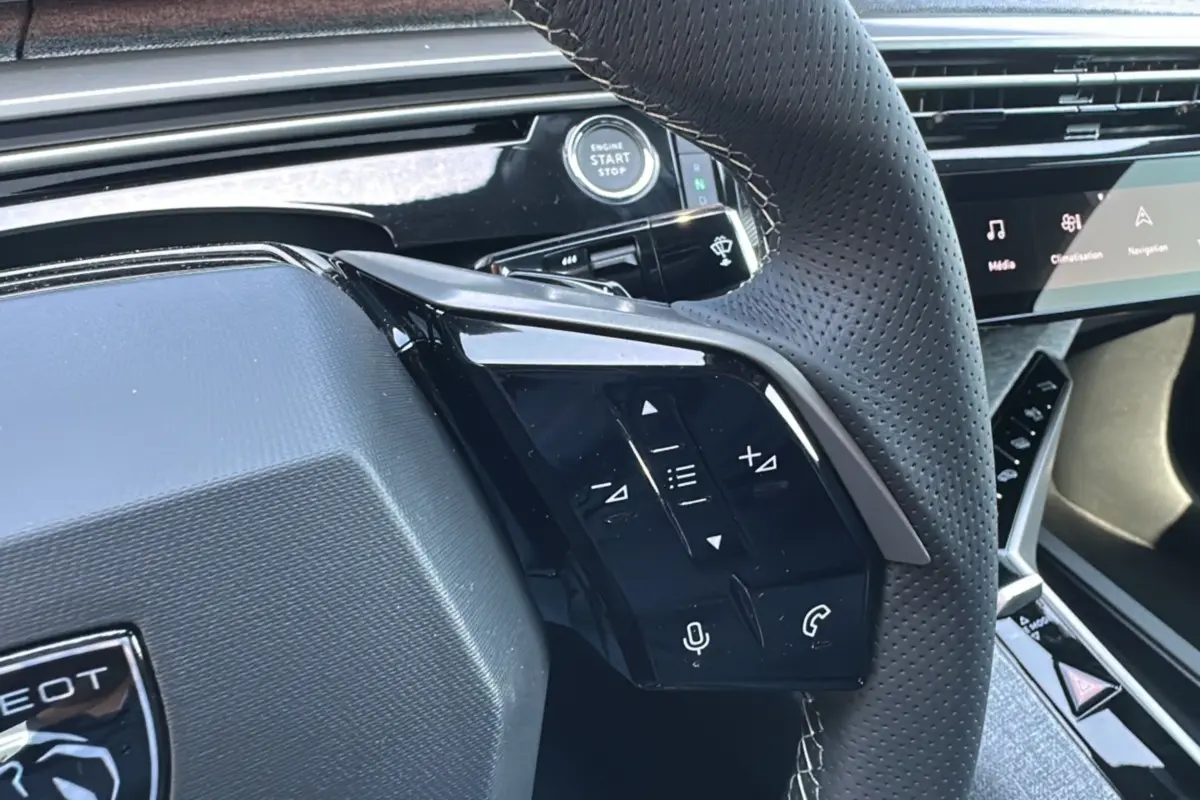 Gros plan sur le volant perforé du Peugeot 3008 Hybrid 2025 avec commandes intégrées et bouton start/stop visible.