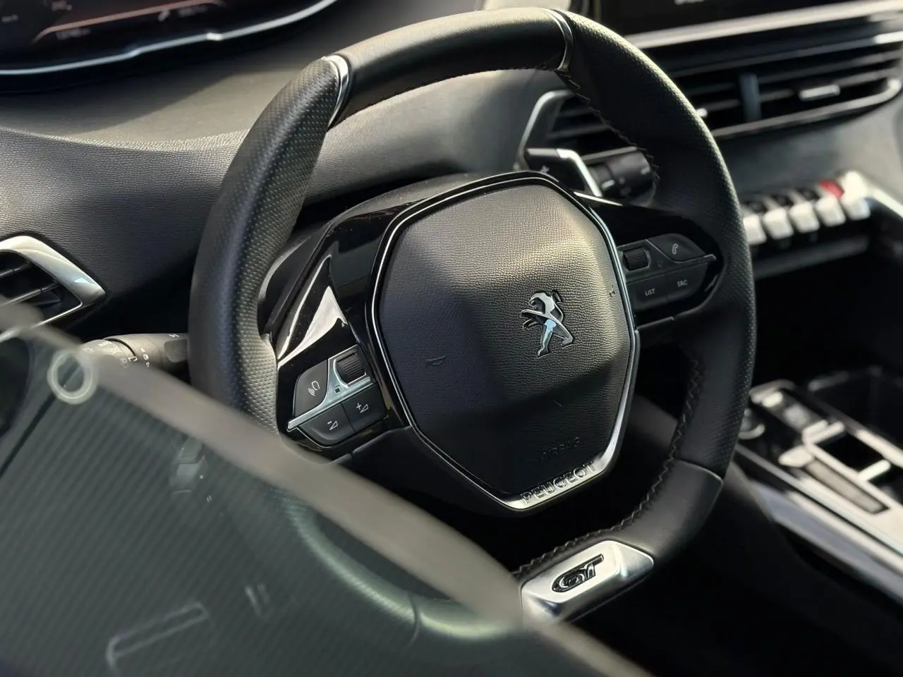 Gros plan sur le volant cuir perforé noir avec logo Peugeot et badge GT dans l’habitacle du 3008 2023.