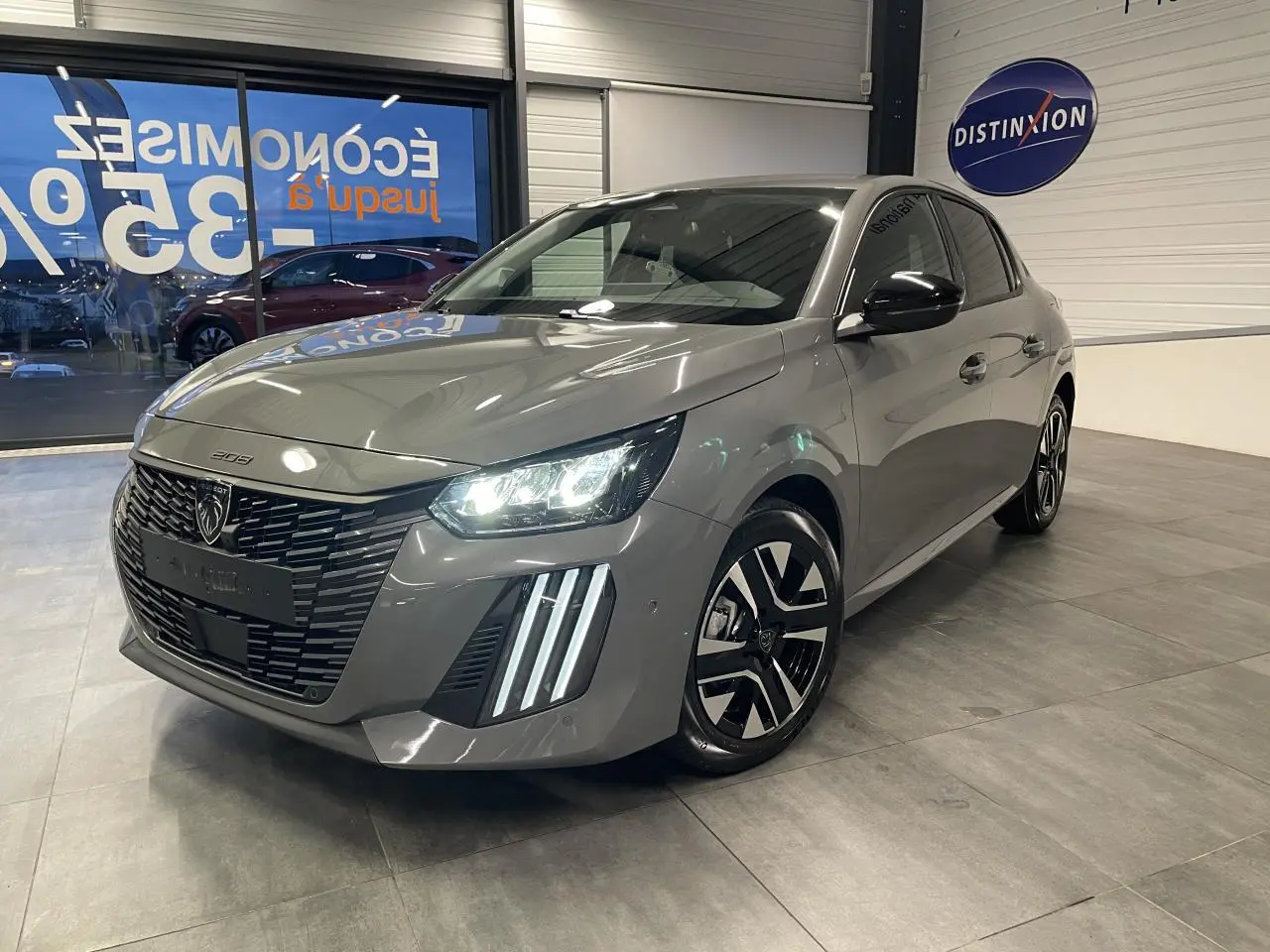 PEUGEOT 208 gris sélénium en vue 3/4 avant droit, avec calandre noire et feux LED à griffes distinctifs.