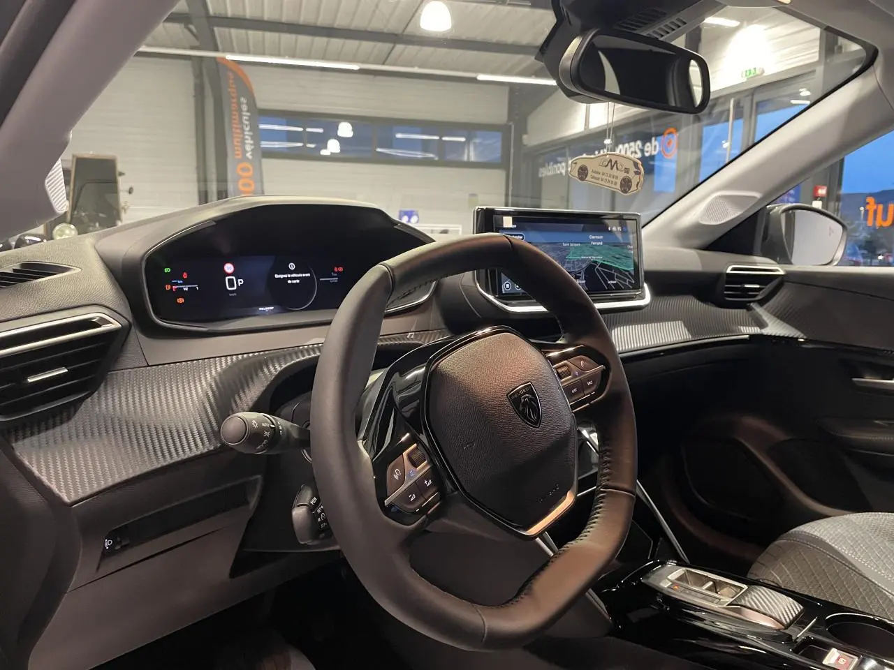 Vue intérieure côté conducteur du Peugeot 208 1.2i Hybrid 2025 avec tableau de bord numérique et volant cuir noir.