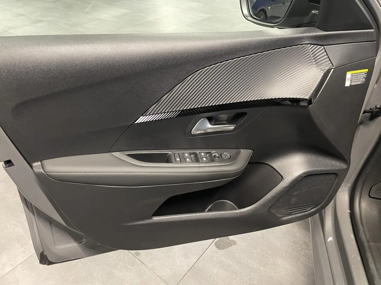 Vue intérieure de la porte avant gauche gris sélénium de la Peugeot 208 Allure avec insert effet carbone et commandes électriques.