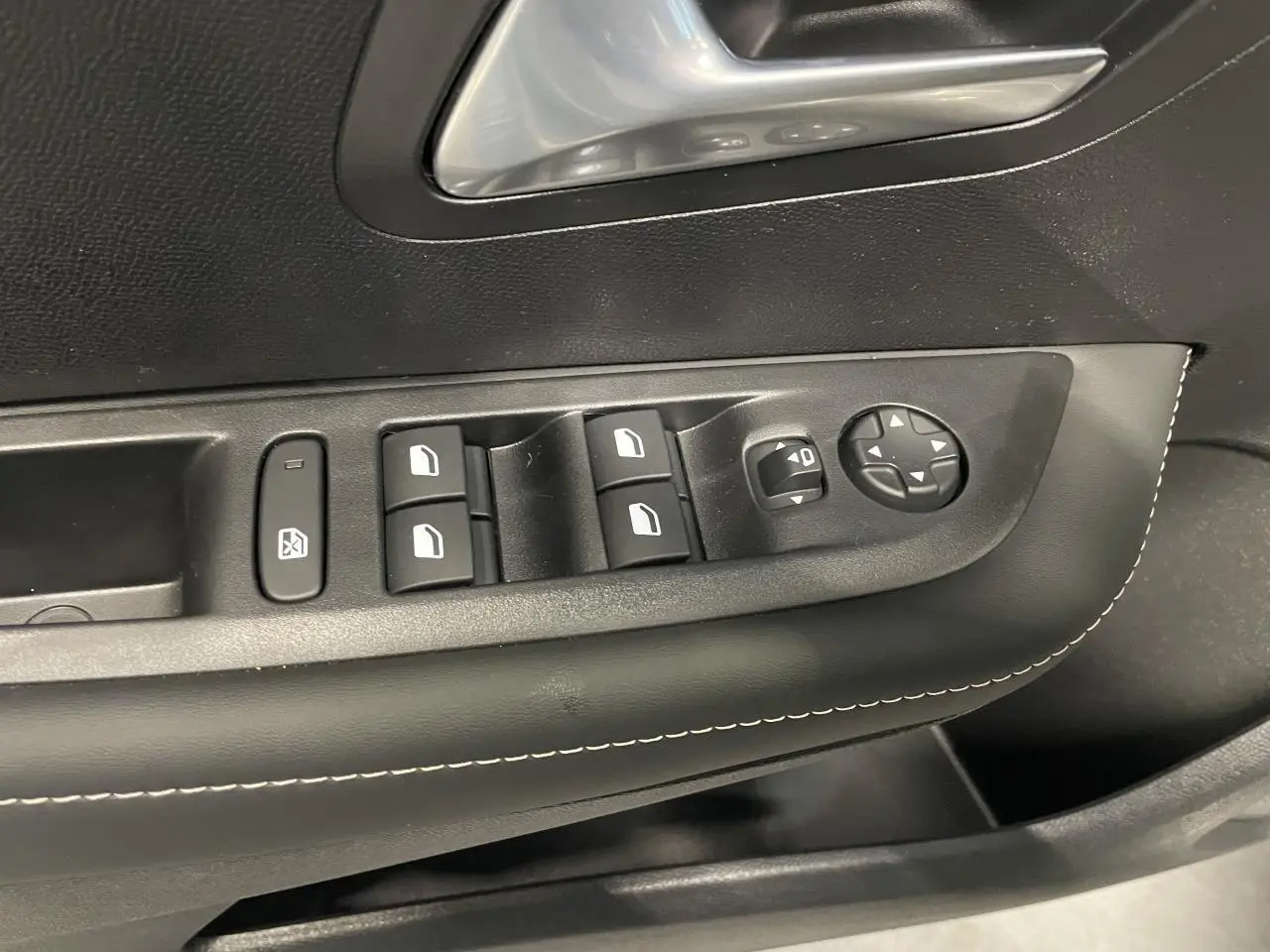 Détail des commandes de lève-vitres et rétroviseurs sur la porte avant gauche d’une Peugeot 208 gris selenium.