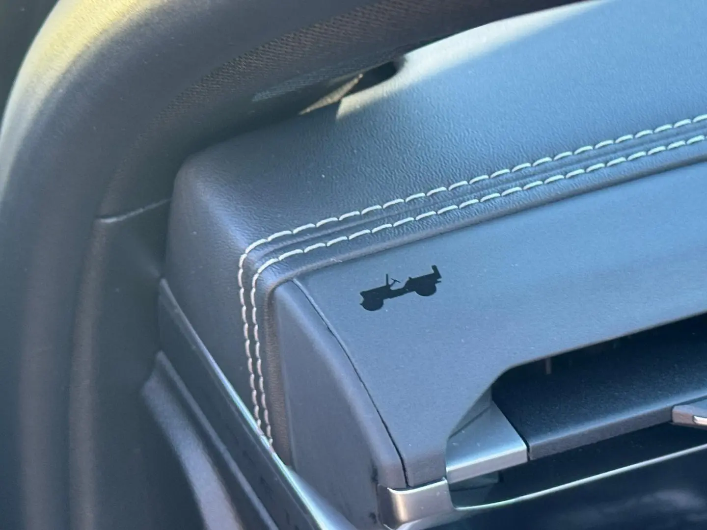 Détail de l'accoudoir central en cuir noir avec surpiqûres blanches et logo Jeep en relief.