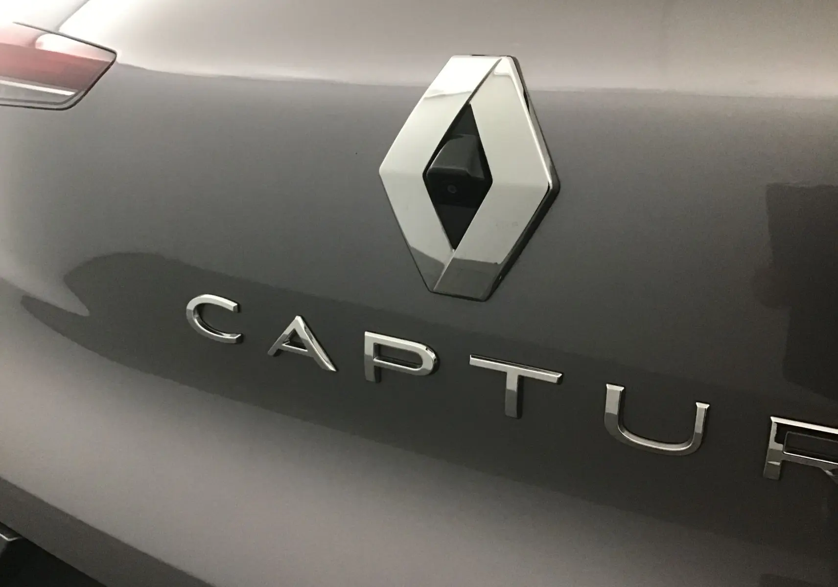 Gros plan sur le logo Renault et l’inscription Captur sur la malle arrière gris cassiopée du SUV 2024.
