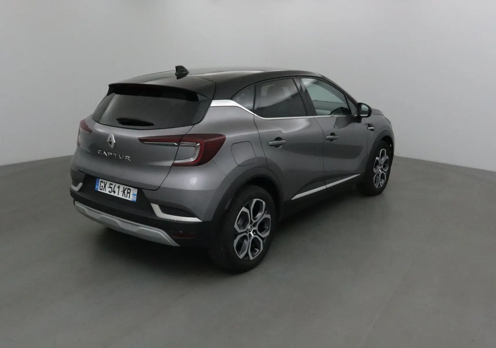 Vue 3/4 arrière droite d'un Renault Captur gris Cassiopée avec toit noir et jantes 18 pouces en studio.