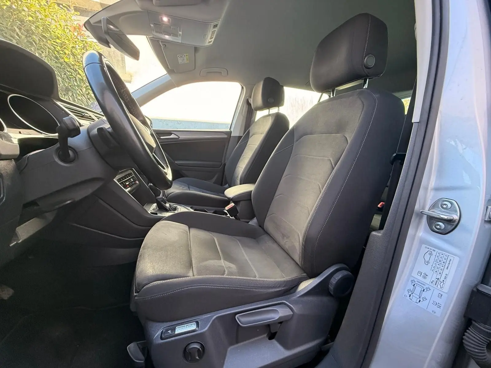 Vue intérieure côté conducteur du Volkswagen Tiguan 2021 avec sièges Ergo Active en tissu noir et portière argentée ouverte.