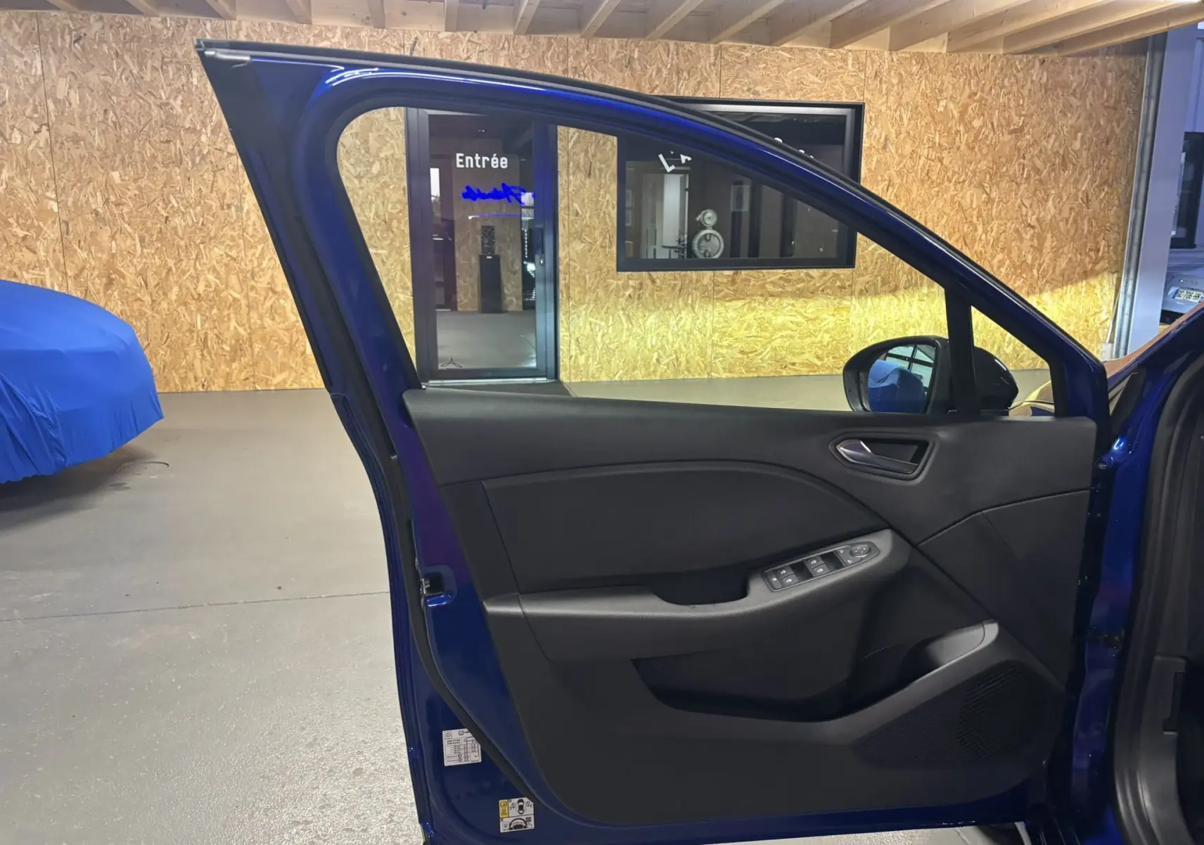 Vue intérieure de la porte avant gauche bleu iron d'une Renault Clio 2024 avec commandes électriques et poignée intégrée.