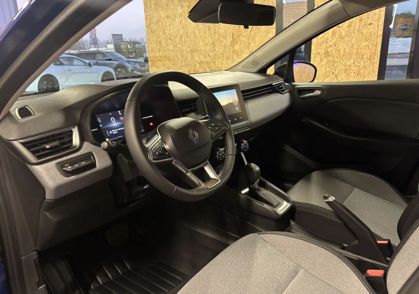 Vue intérieure côté conducteur de la Renault Clio TCE 90CH X-TRONIC Evolution 2024 avec tableau de bord numérique et sièges tissu gris-noir.