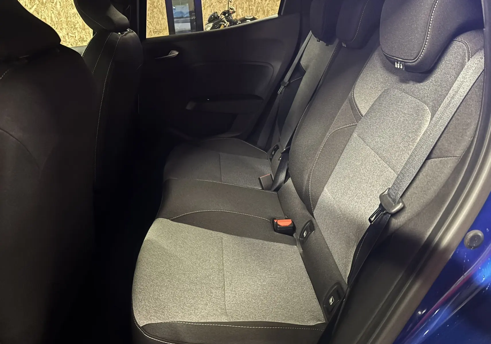 Vue intérieure côté droit des sièges arrière en tissu gris et noir d'une Renault Clio 2024 bleu Iron avec ceinture de sécurité visible.