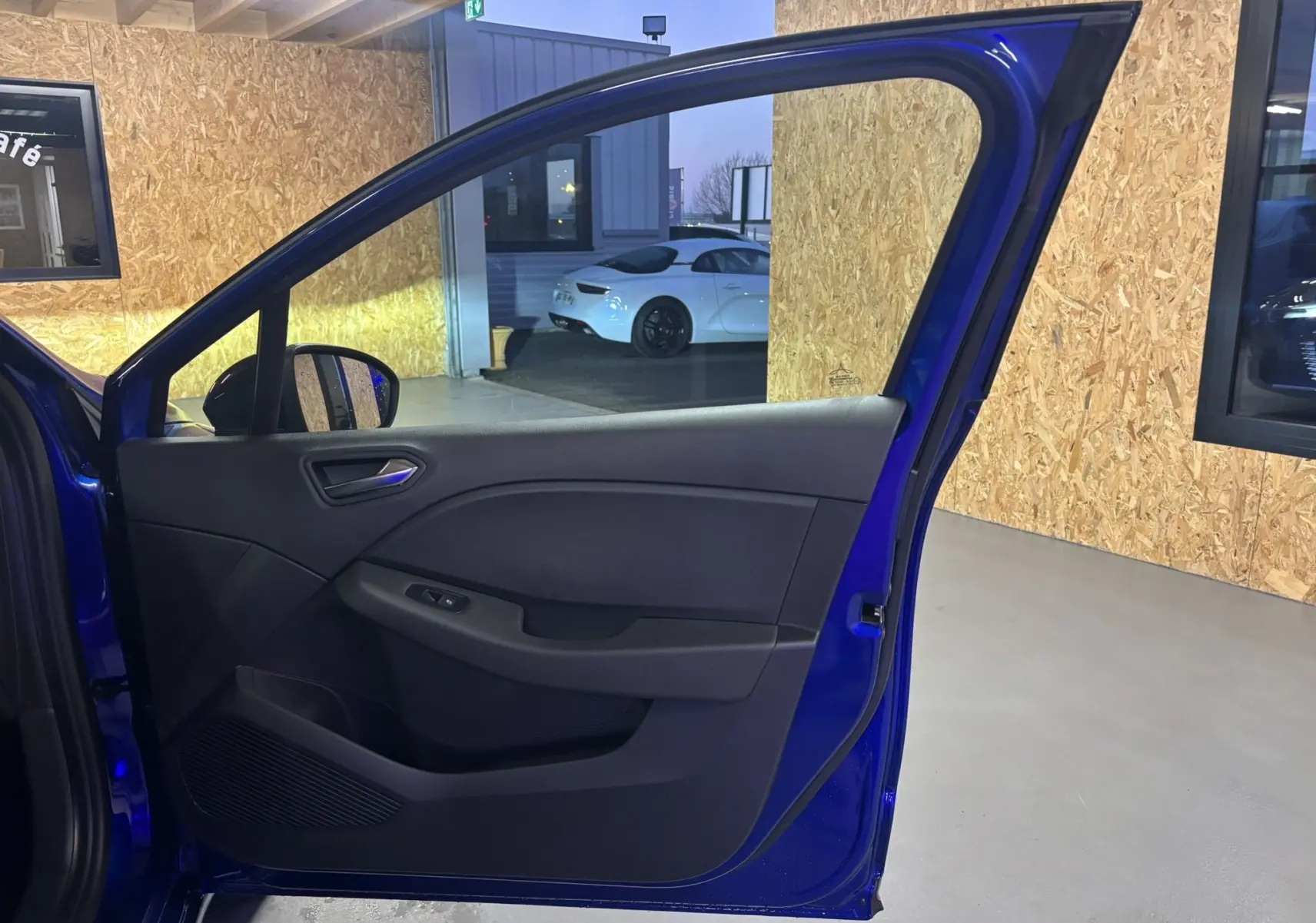 Porte avant gauche ouverte d'une Renault Clio 2024 bleu iron, montrant l'habillage intérieur noir et les commandes de fenêtre.