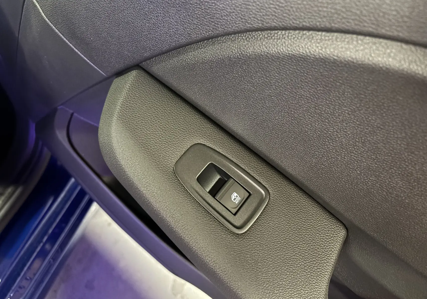 Bouton de commande de lève-vitre sur la porte intérieure côté conducteur d'une Renault Clio bleu iron 2024.