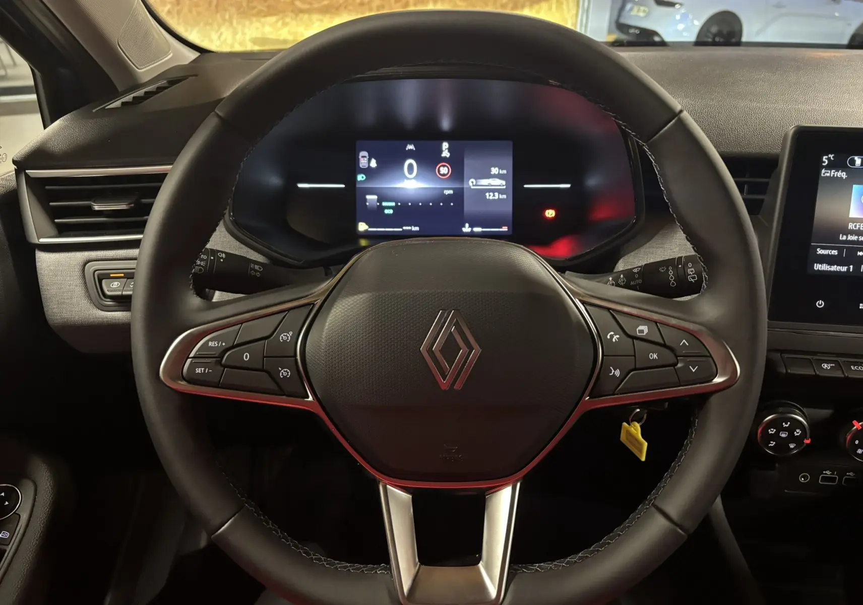 Vue rapprochée du volant noir de la Renault Clio 2024 avec commandes intégrées et tableau de bord digital allumé.