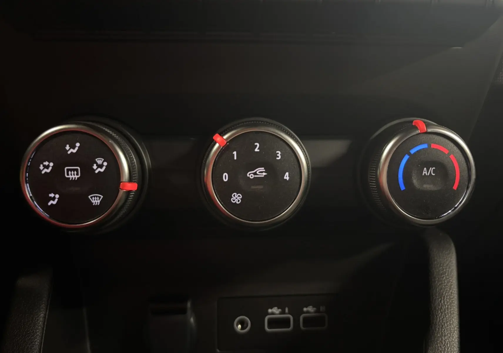 Commandes de climatisation avec trois molettes noires et détails rouges à l'intérieur d'une Renault Clio bleu Iron 2024.