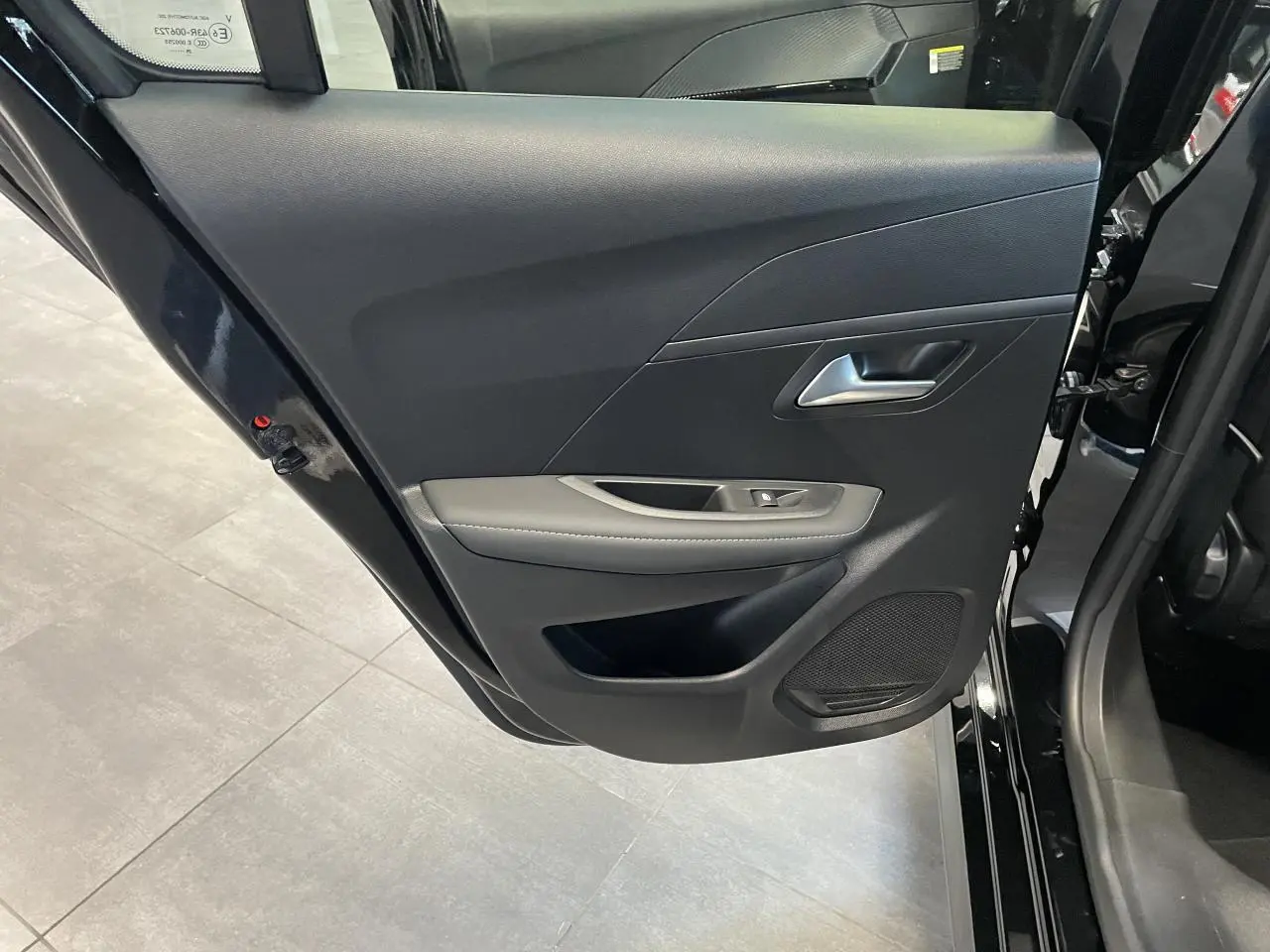 Vue rapprochée de la porte arrière gauche noire du Peugeot 208 2025 avec garniture grise et haut-parleur intégré.