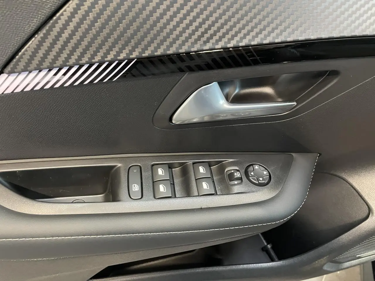 Détail de la porte avant gauche noire de la Peugeot 208 1.2i Hybrid avec commandes de vitres et rétroviseurs.