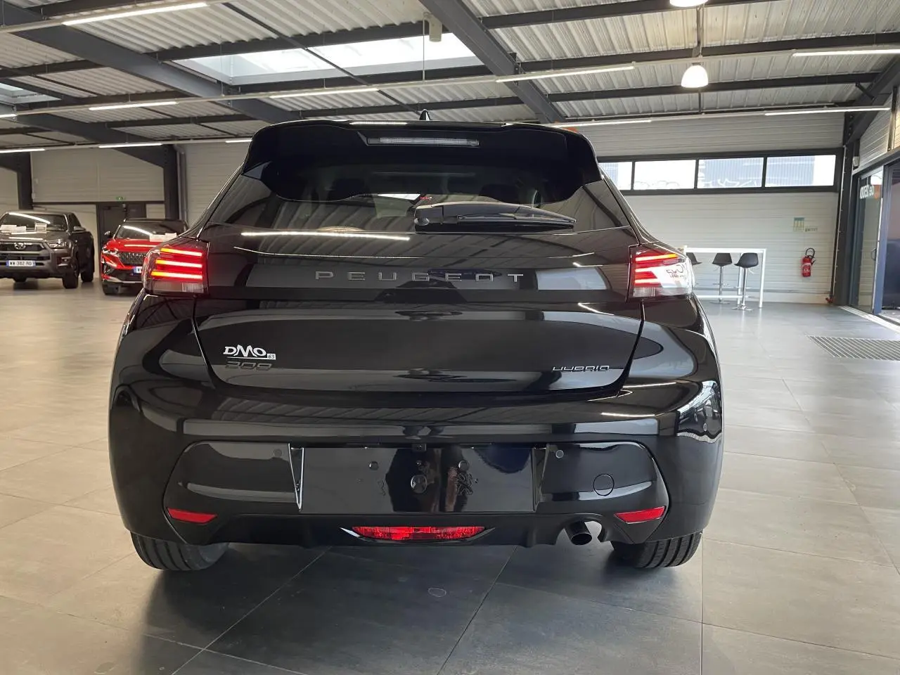 Vue arrière d'une Peugeot 208 noire avec feux arrière à LED en forme de griffes dans un showroom.