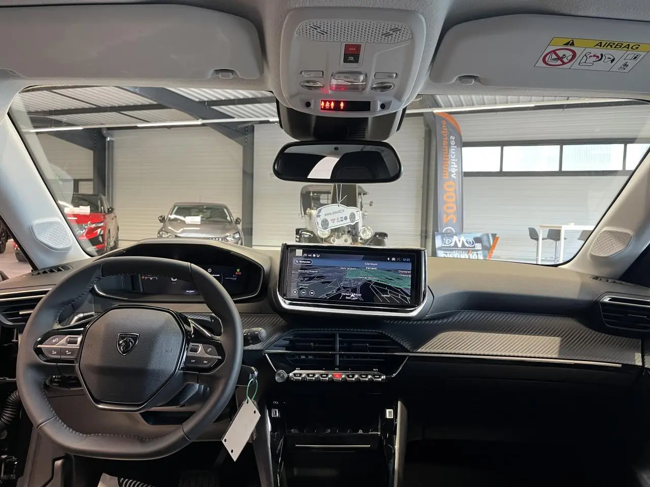 Vue intérieure avant du Peugeot 208 noir hybride 2025, mettant en valeur le tableau de bord avec écran tactile et volant compact cuir.