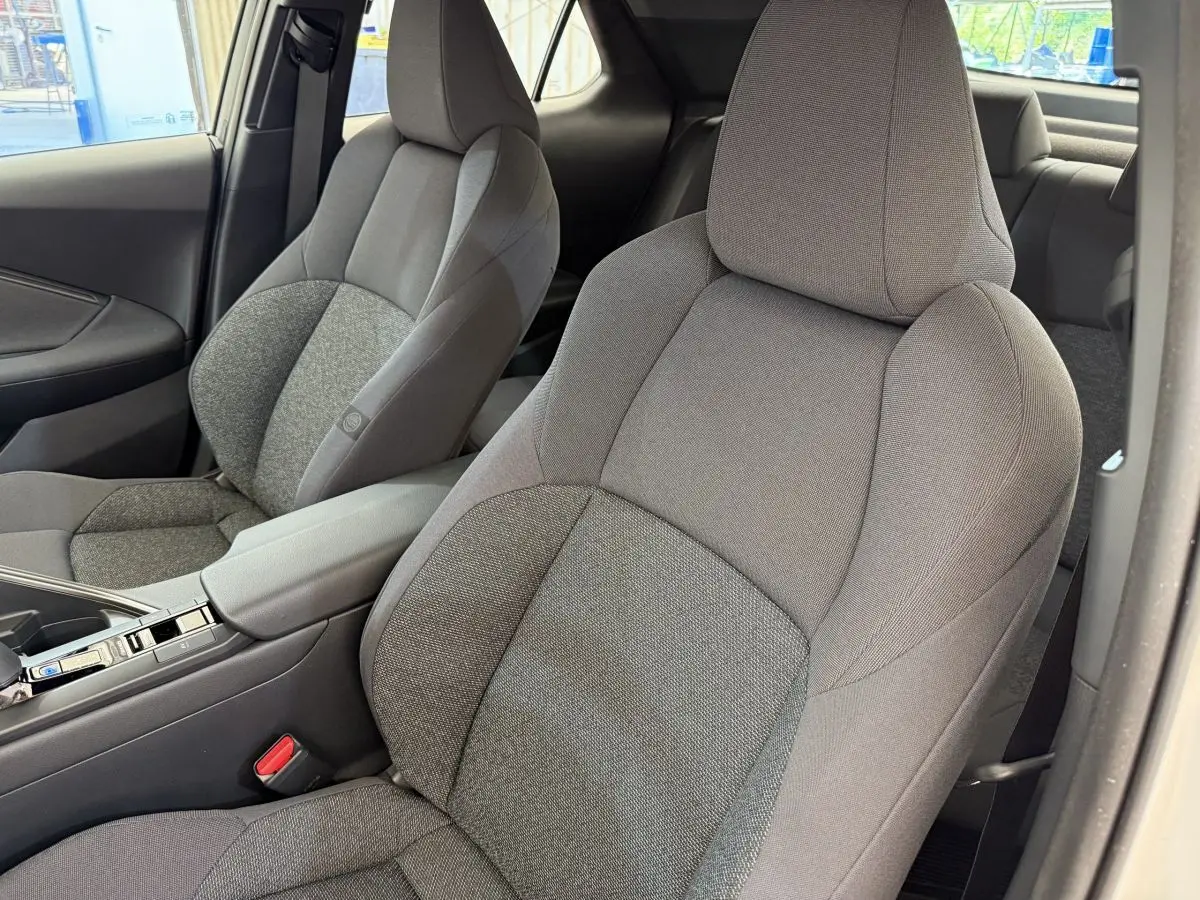 Vue intérieure rapprochée des sièges avant gris du Toyota C-HR 1.8 Hybride 140 Dynamic, avec accoudoir central.
