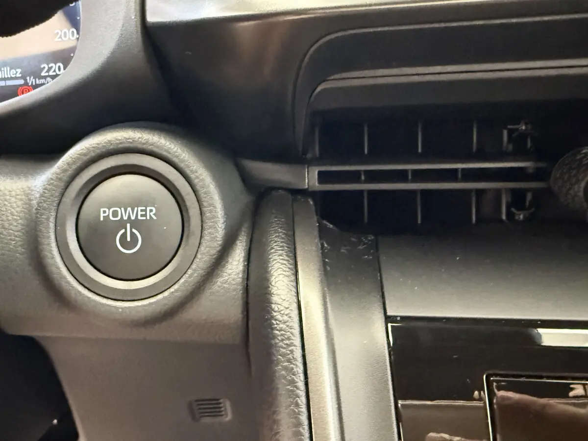 Gros plan sur le bouton Power noir du tableau de bord du Toyota C-HR 1.8 Hybride blanc, avec sortie d'air à droite.