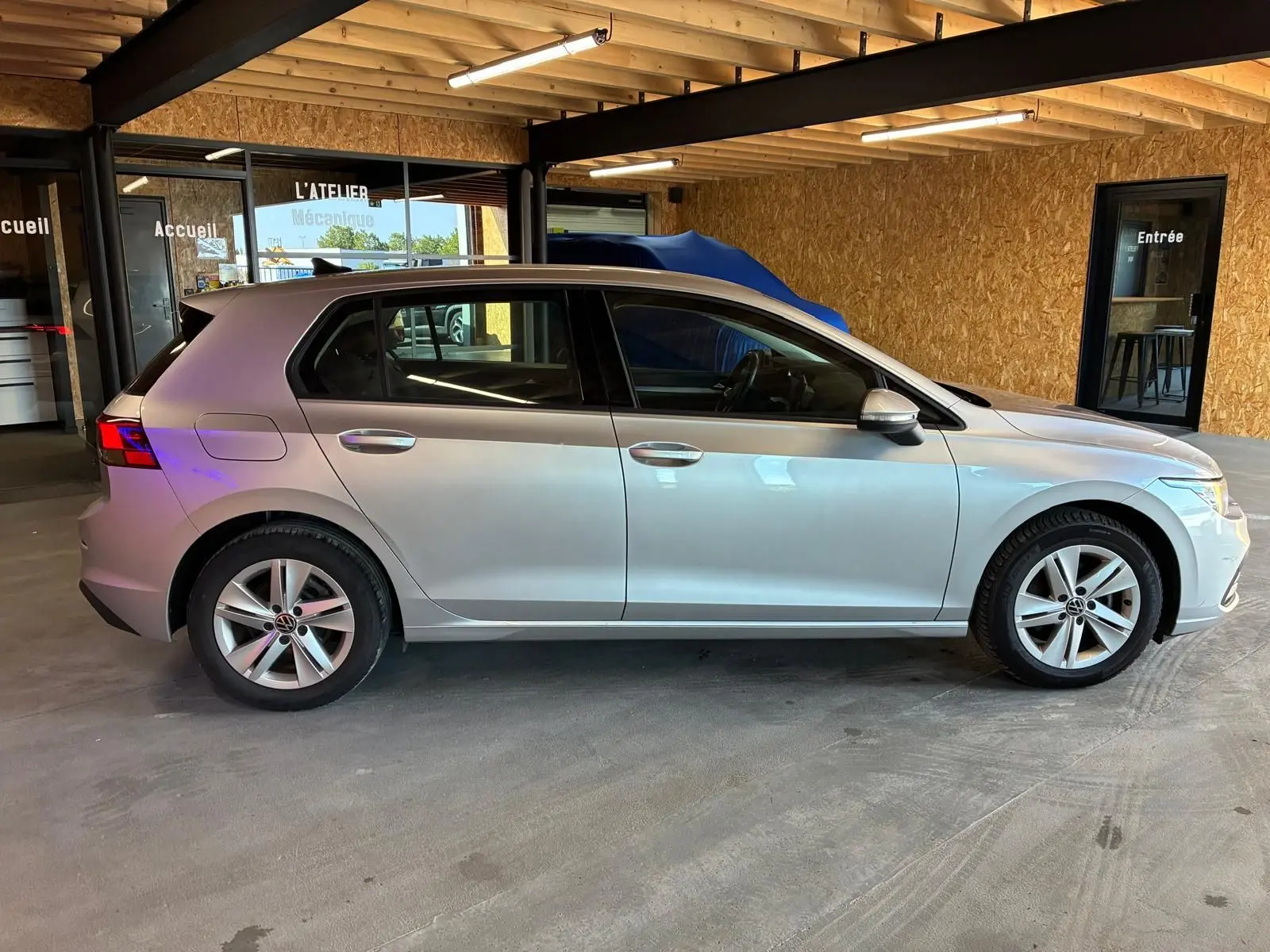 Vue de profil côté gauche d'une Volkswagen Golf 1.0 eTSI 110 DSG7 Life Plus gris clair, stationnée en intérieur.