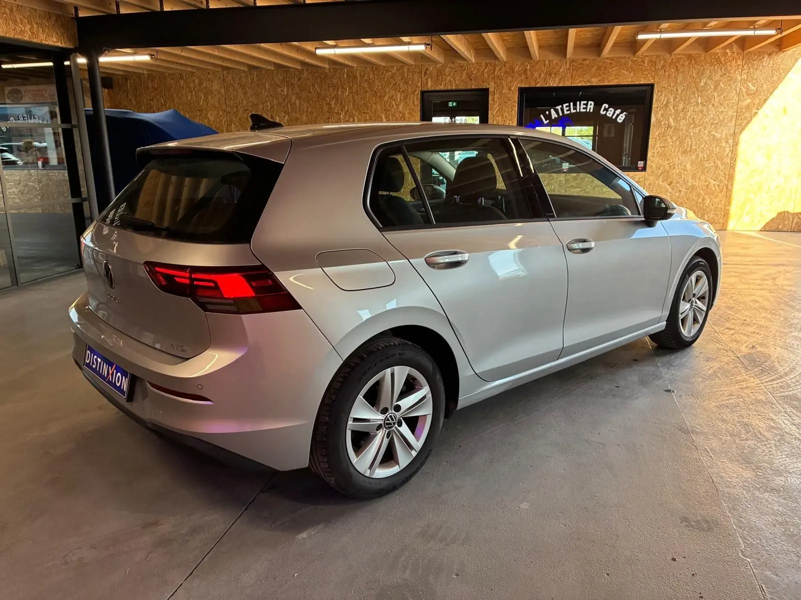 Volkswagen Golf 1.0 eTSI 110 DSG7 gris clair vue 3/4 arrière droit en intérieur avec feux arrière allumés.