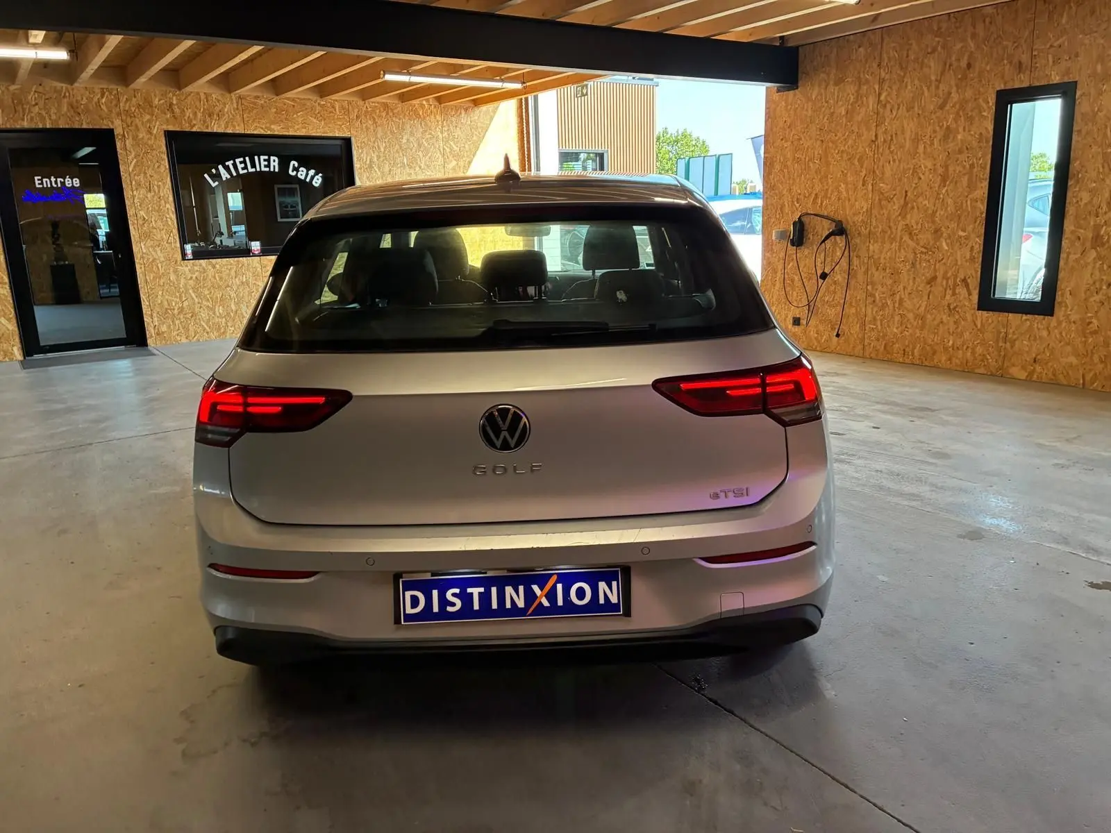 Vue arrière d'une Volkswagen Golf gris clair 2023 avec feux LED allumés, stationnée dans un garage lumineux.