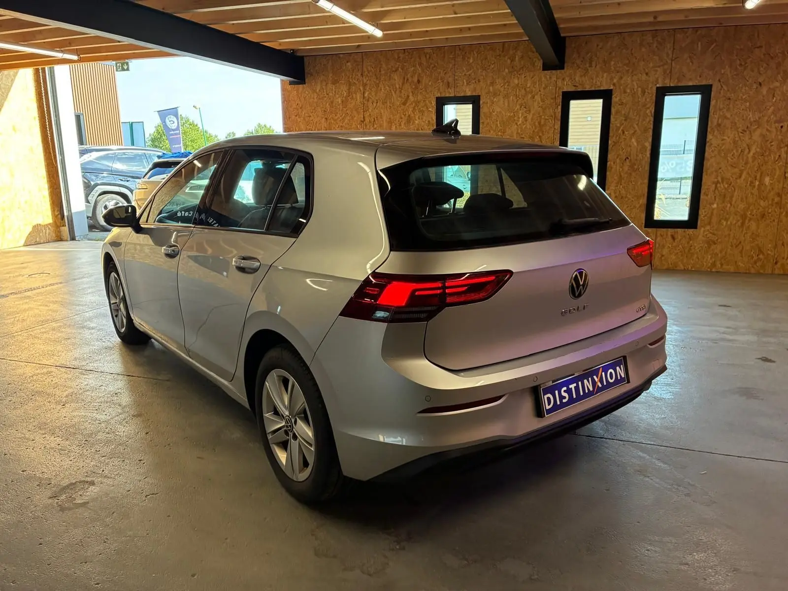 Volkswagen Golf gris clair 2023 vue 3/4 arrière droit avec feux arrière allumés en intérieur.