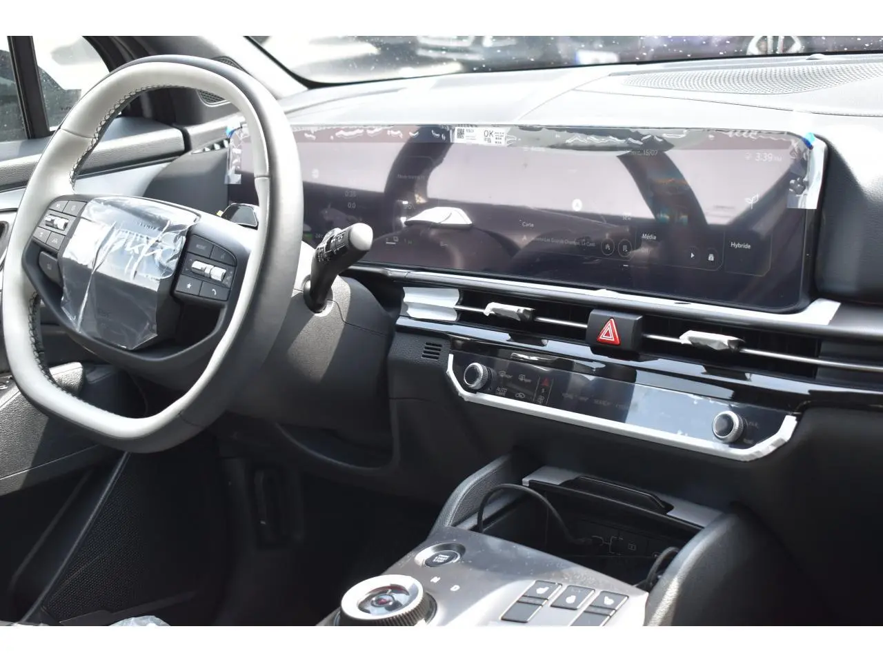 Vue intérieure côté conducteur du tableau de bord du Kia Sportage hybride gris avec écran digital large et volant multifonction.