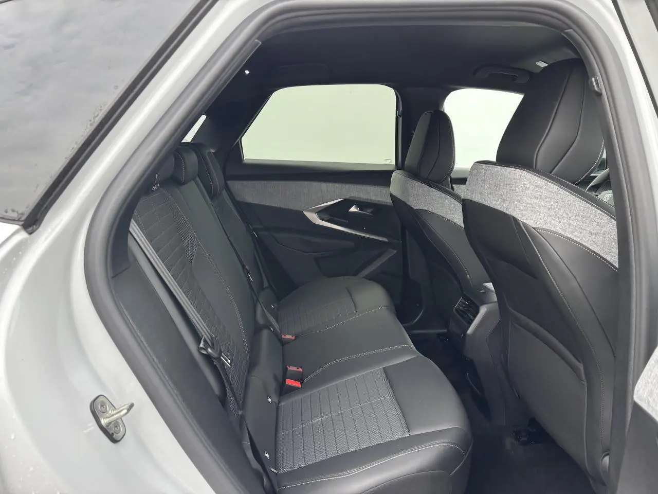 Vue intérieure arrière côté gauche du Peugeot 3008 blanc Okenite 2024 avec sellerie mixte tissu et cuir noir.