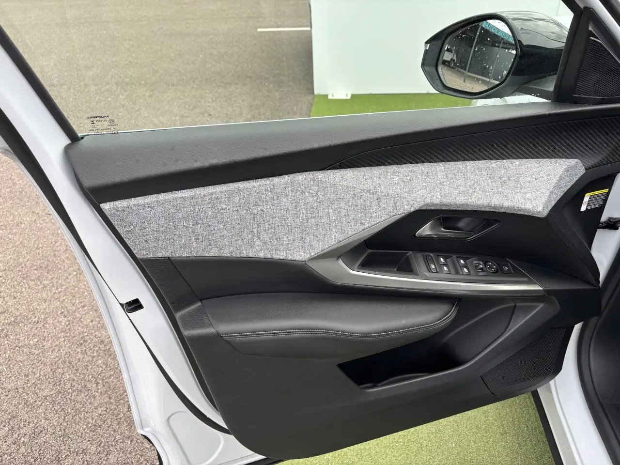 Porte avant gauche ouverte d'un Peugeot 3008 blanc Okenite, montrant le panneau avec commandes et décor tissu gris chiné.