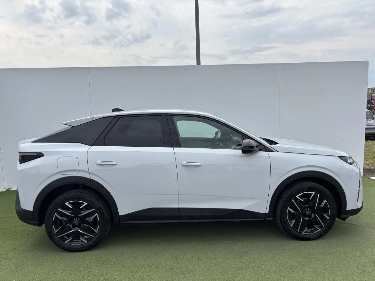 Profil droit du Peugeot 3008 blanc Okenite 2024 avec jantes alliage noires et toit noir contrasté.