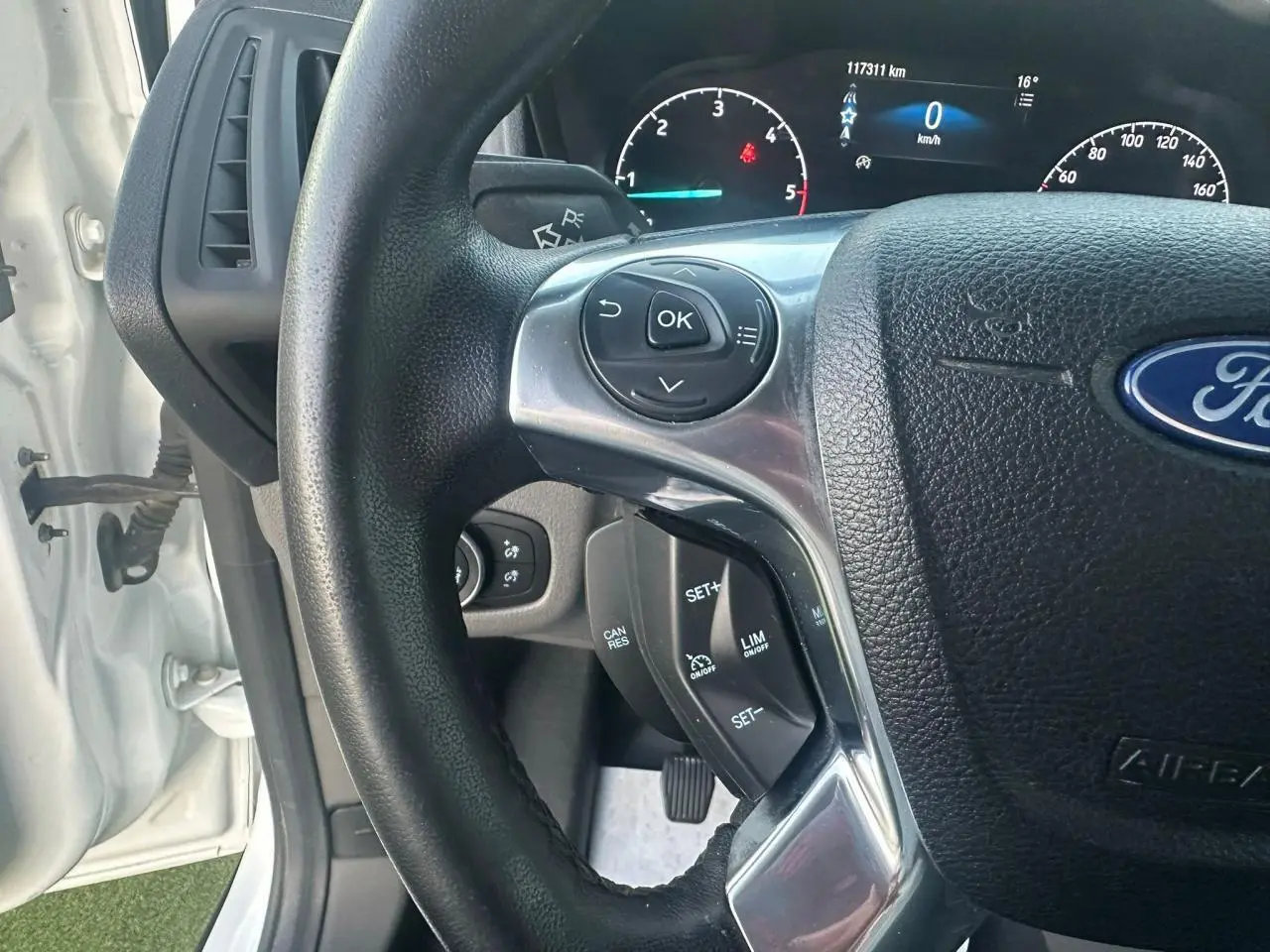 Vue rapprochée du volant multifonction noir du Ford Transit Connect blanc, avec tableau de bord digital en arrière-plan.