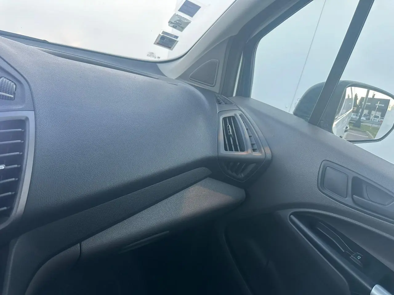 Vue intérieure côté passager du tableau de bord noir du Ford Transit Connect blanc avec aérateurs angulaires.