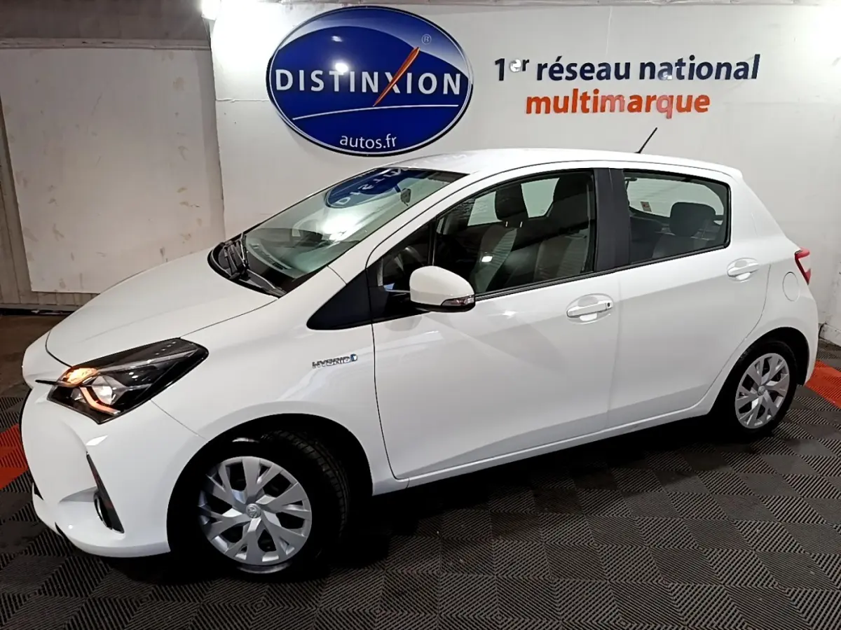 Vue de profil droit d'une Toyota Yaris 1.5 Hybride blanche avec feux avant allumés dans un showroom.